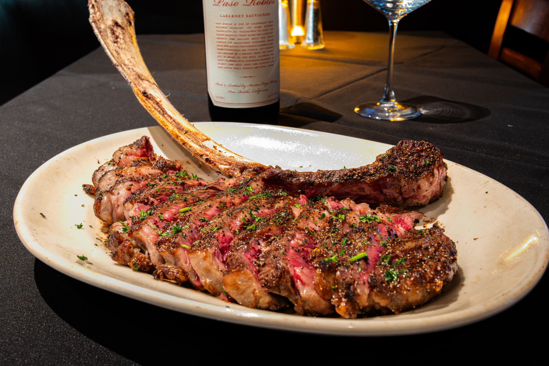 A sliced tomahawk steak on a plate with a bottle of Cabernet Sauvignon